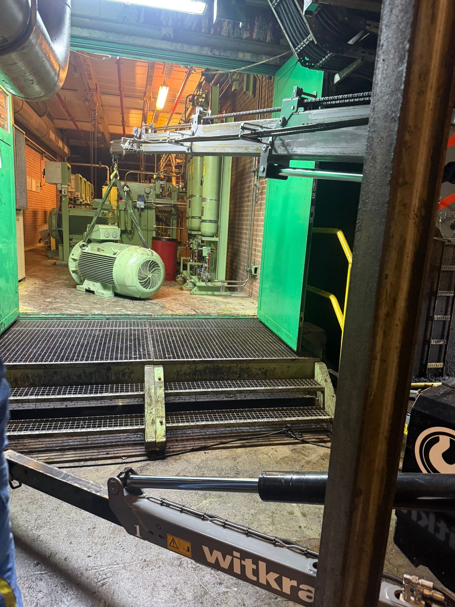 Elektrische minikraan hijst zware elektromotor in een fabriekshal binnenshuis