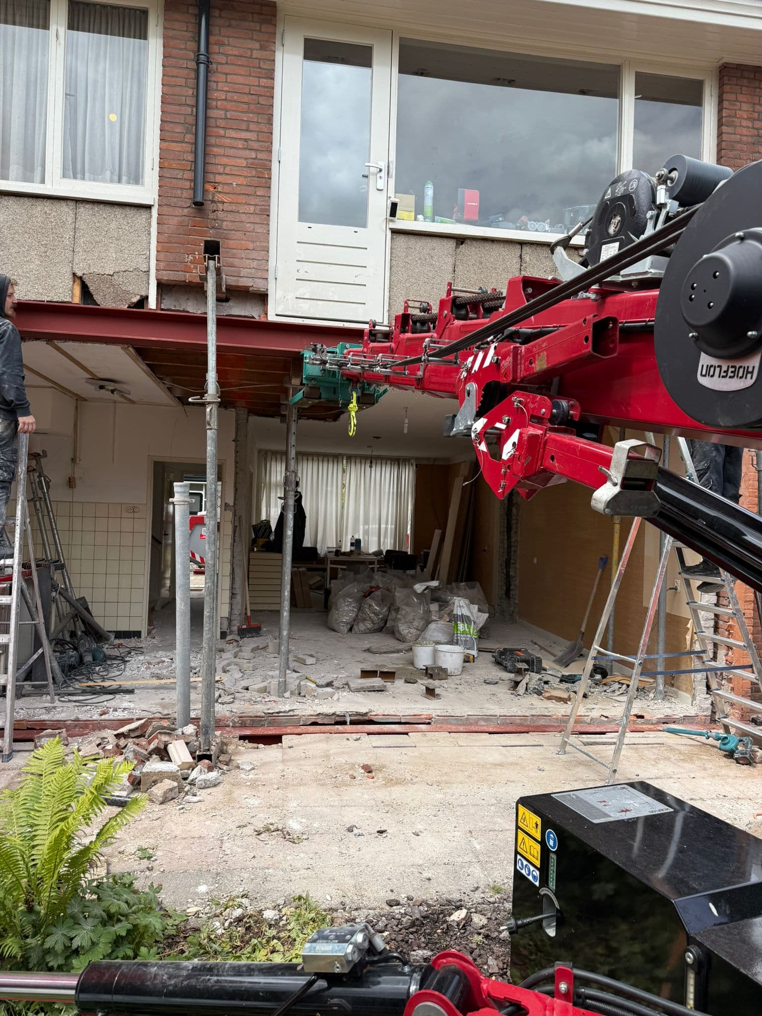 Minikraan plaatst een zware stalen balk bij een woningrenovatie binnenshuis